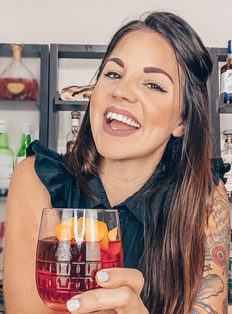 Jacki Schromm smiling and holding up a cocktail