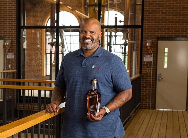 Tony Burke standing in the Angel's Envy distillery, holding a bottle of Angel's Envy bourbon