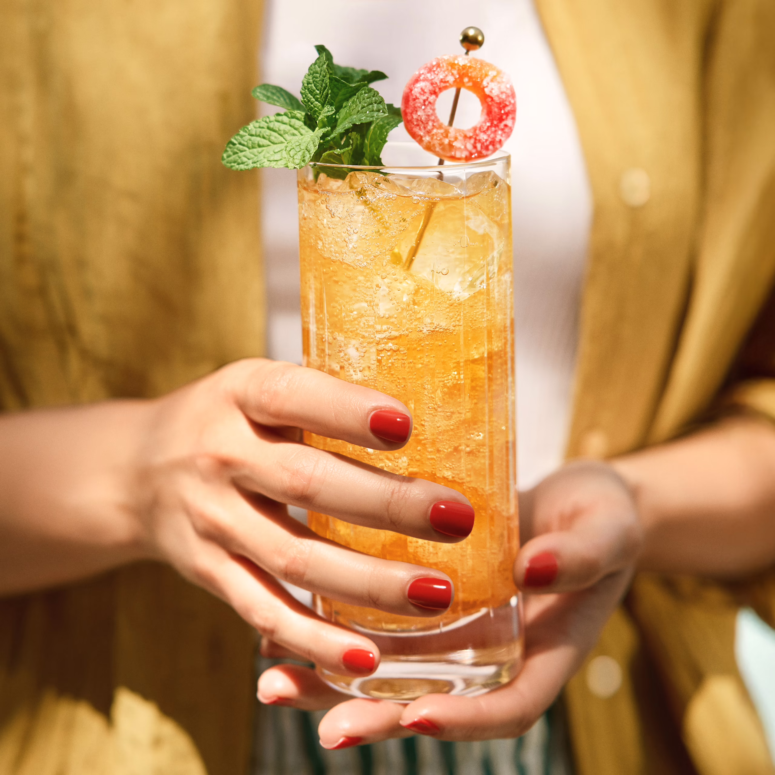 A refreshing Angel’s Envy Peach Smash cocktail held by a woman wearing summer attire in the warm sunlight.