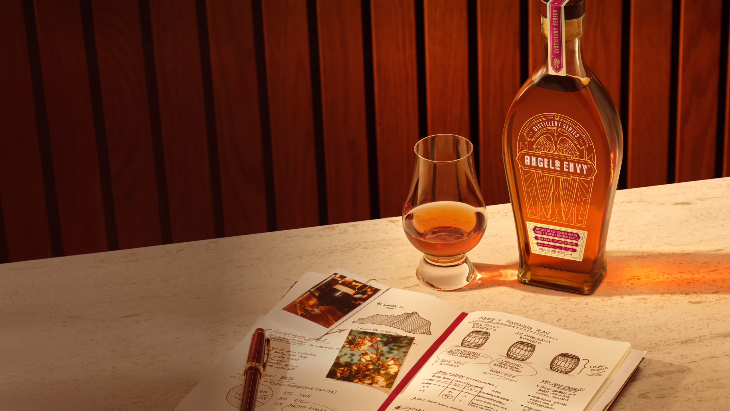 A bottle of Angel’s Envy Distillery Series Whiskey beside a tasting glass and an open notebook filled with handwritten tasting notes and photographs.