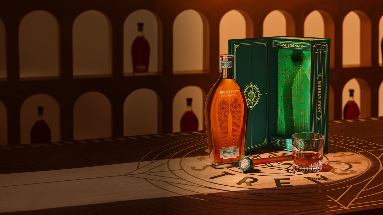 The Angel’s Envy 10 Cask Strength Rye bottle, the limited-edition presentation box in emerald green and gold, and a glass of whiskey displayed together on a logo-engraved table in the Cask Archives room.