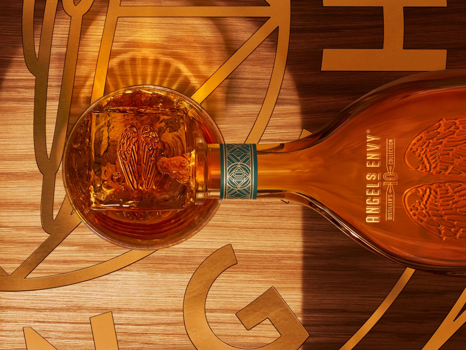Overhead view of the Angel’s Envy 10 Cask Strength Rye bottle being poured into a whiskey glass on a logo-engraved table in the Cask Archives room.