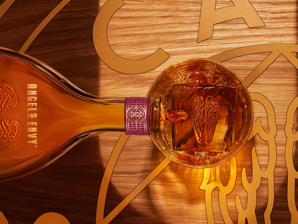 Overhead view of the the Angel’s Envy 2026 Cask Strength Bourbon bottle being poured into a whiskey glass on a logo-engraved table in the Cask Archives room.