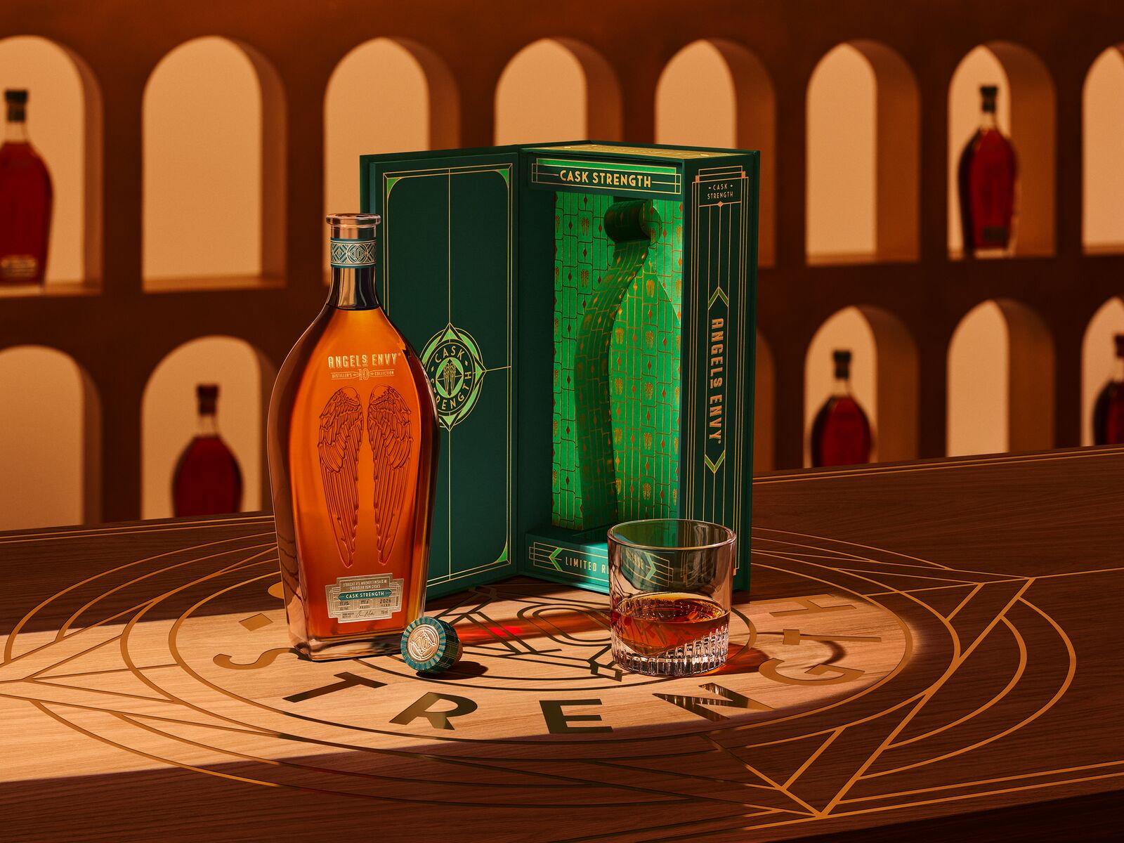 The Angel’s Envy 10 Cask Strength Rye bottle, the limited-edition presentation box in emerald green and gold, and a glass of whiskey displayed together on a logo-engraved table in the Cask Archives room.
