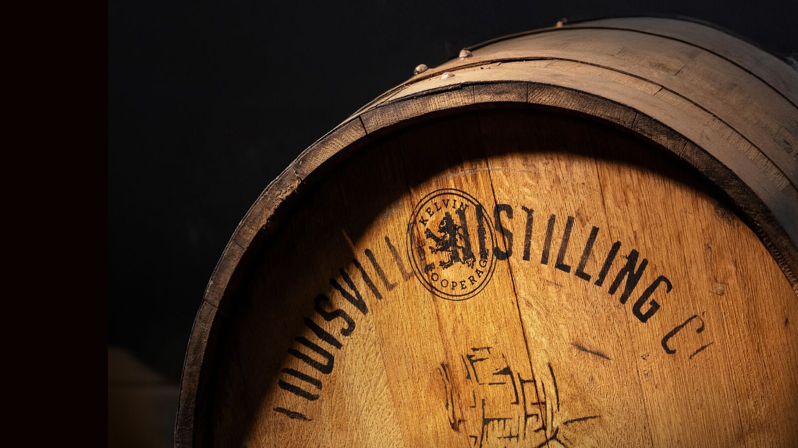 A warmly lit close-up of an Angel’s Envy oak barrel with a cascading shadow.