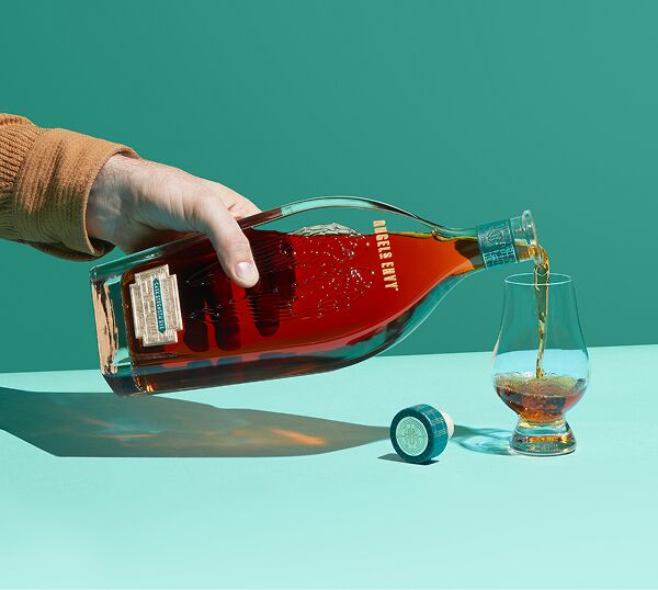Master Distiller Owen Martin pouring a tasting glass from a bottle of Angel’s Envy Cask Strength Rye 1st Edition in front of a two-toned turquoise background.