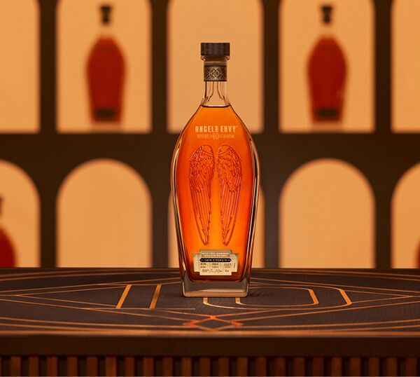 A spotlit bottle of Angel’s Envy 10 Cask Strength Bourbon presented on a black and gold logo-lit table within the Cask Archives room.