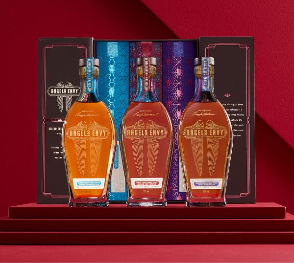 The three 375 mL bottles and the book-inspired presentation box from the limited-edition Angel’s Envy Cellar Collection Vol. 1-3 release featuring a colorful Angel’s Envy on top of a red staged platform.