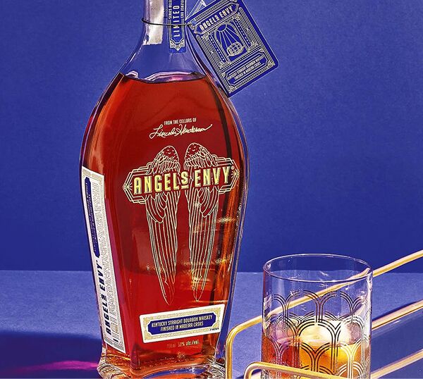 The Cellar Collection Vol. 3 bottle with an intricately-detailed blue bottle tag and an art deco rocks glass on a golden drink tray, presented in front of a tonal background.