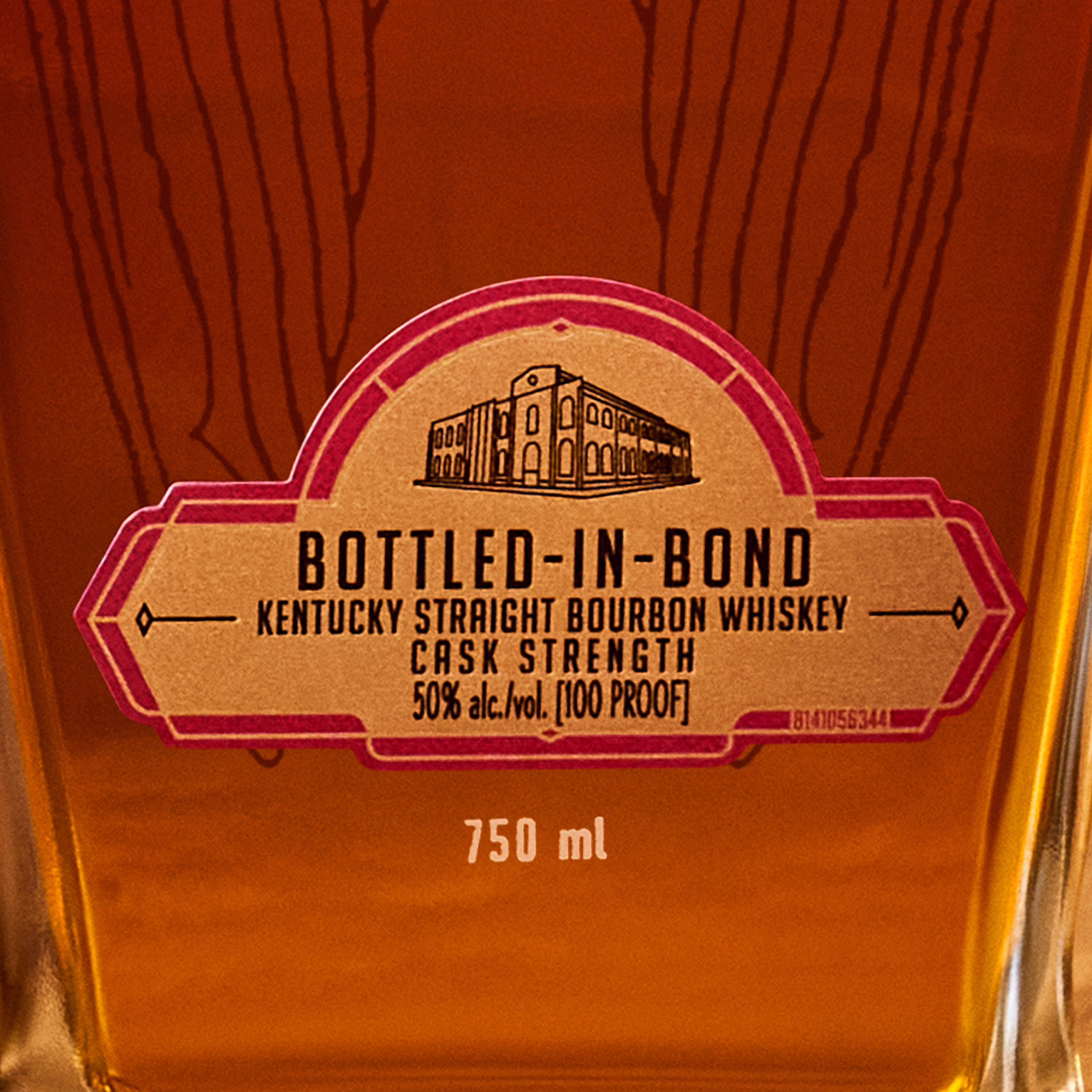 A close-up of the Angel’s Envy Cask Strength Bottled-in-Bond bourbon bottle label in gold, featuring a graphic of the distillery and a ruby art deco trim.