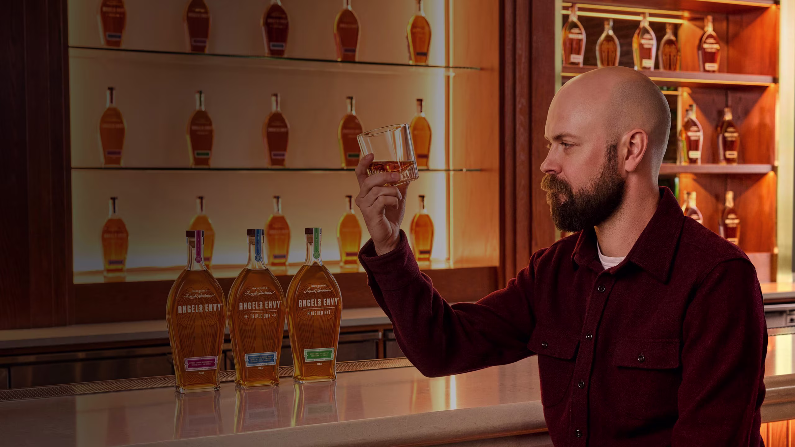 Master Distiller Owen Martin looking at a tasting glass in front of a beautifully-lit bar inside the Angel’s Envy Distillery in Louisville, Kentucky.
