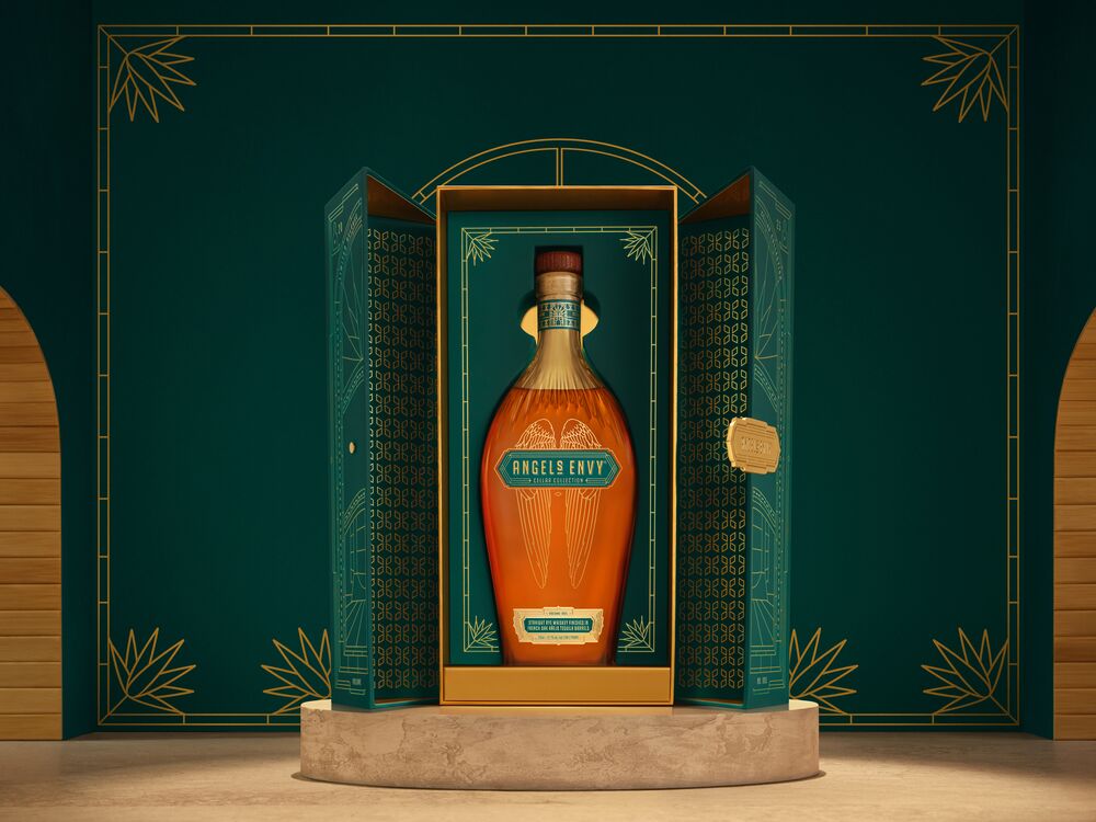 The Angel’s Envy Cellar Collection Vol. 5 bottle, displayed with its emerald green and gold presentation box on a textured stone pedestal against a deep green architectural backdrop.