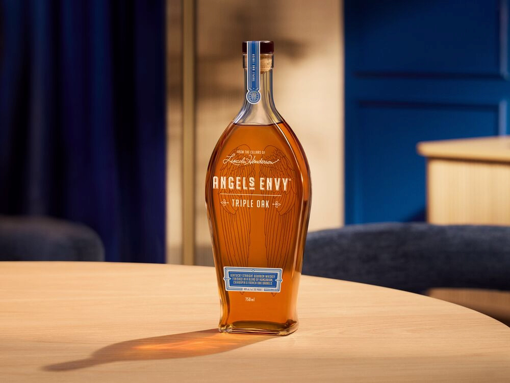 A bottle of Angel’s Envy bourbon on a wooden table against a softly lit blue interior.