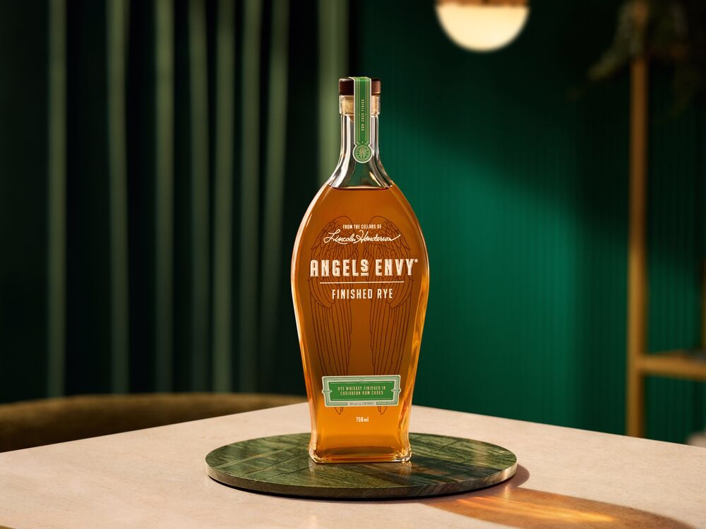 A bottle of Angel’s Envy Rum-Finished Rye displayed on a jade saucer. It’s placed in front of a green wall with golden accents.