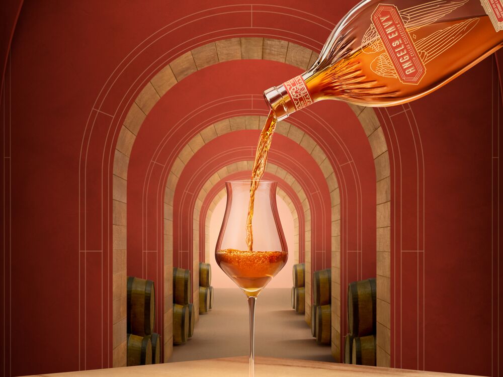 Angel’s Envy Cellar Collection Rye being poured into a stemmed tasting glass in a red corridor with oak arches, and whiskey barrels in the background.