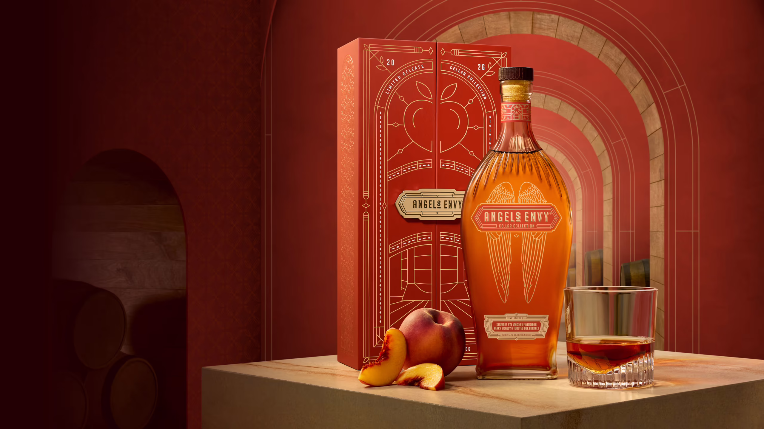 A bottle of Cellar Collection Rye sitting in front of a red decorative Angel’s Envy presentation box next to a rocks glass and peaches against a warm red backdrop.