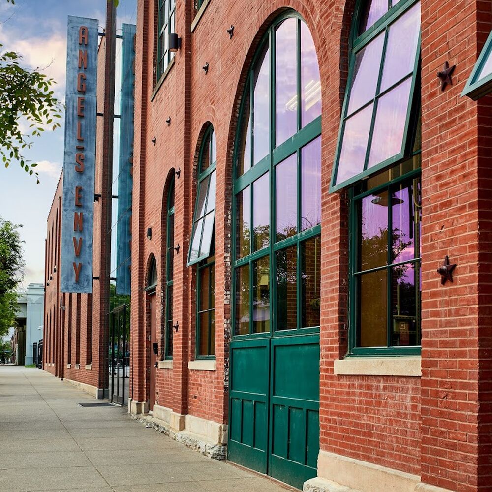 Exterior of the Angel’s Envy Distillery, featuring a red brick wall, tall arched windows, and a vertical Angel’s Envy sign.
