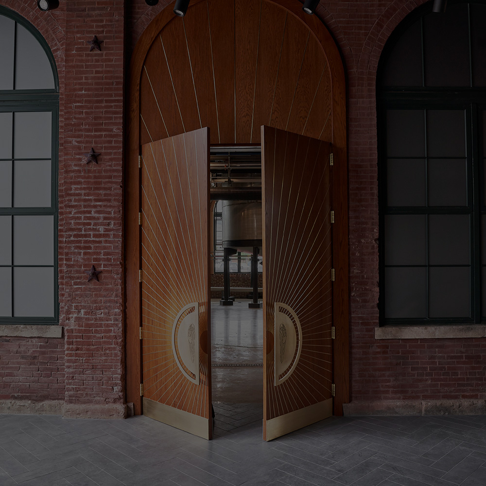A set of gold-plated, wooden double doors, resting ajar and revealing a view inside the Angel’s Envy distillery.