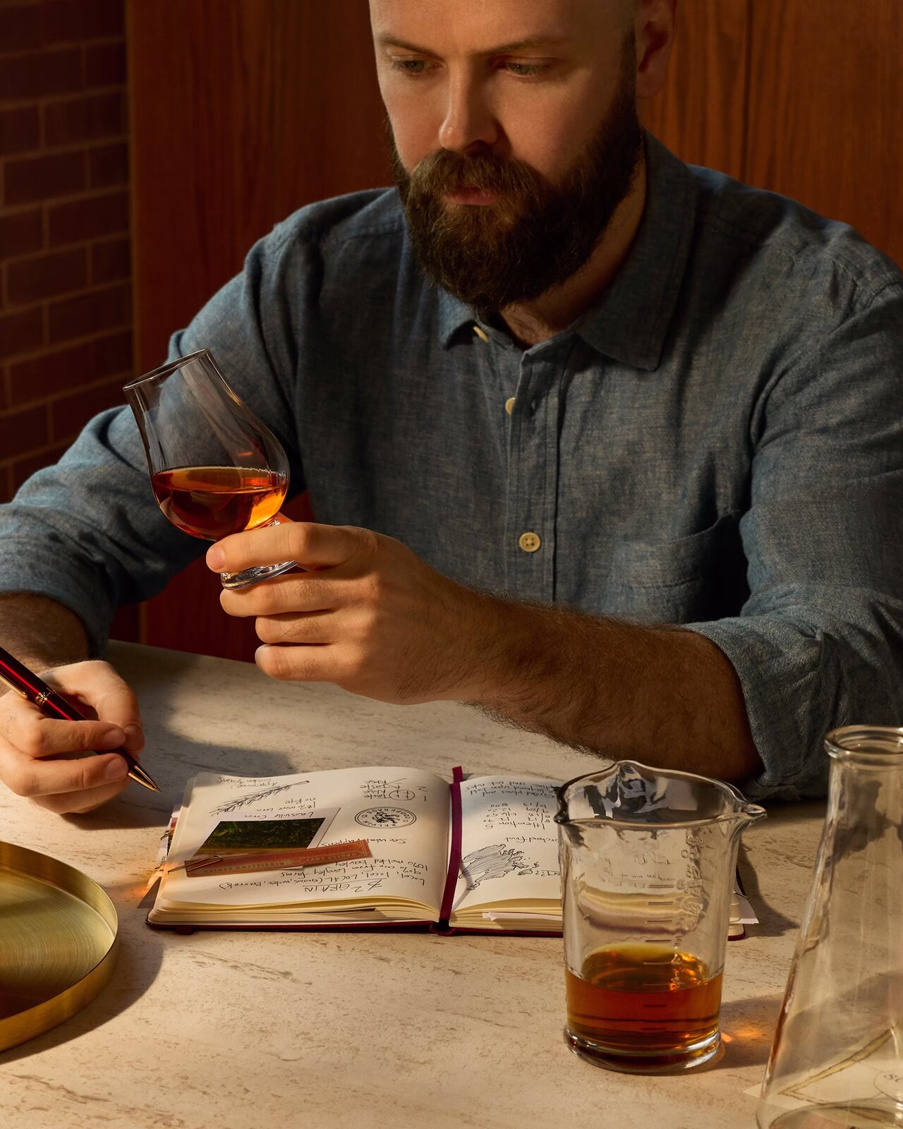 Master Distiller Owen Martin evaluating a glass of whiskey while taking tasting notes in his notebook. A beaker with whiskey sits on the table in front of him.