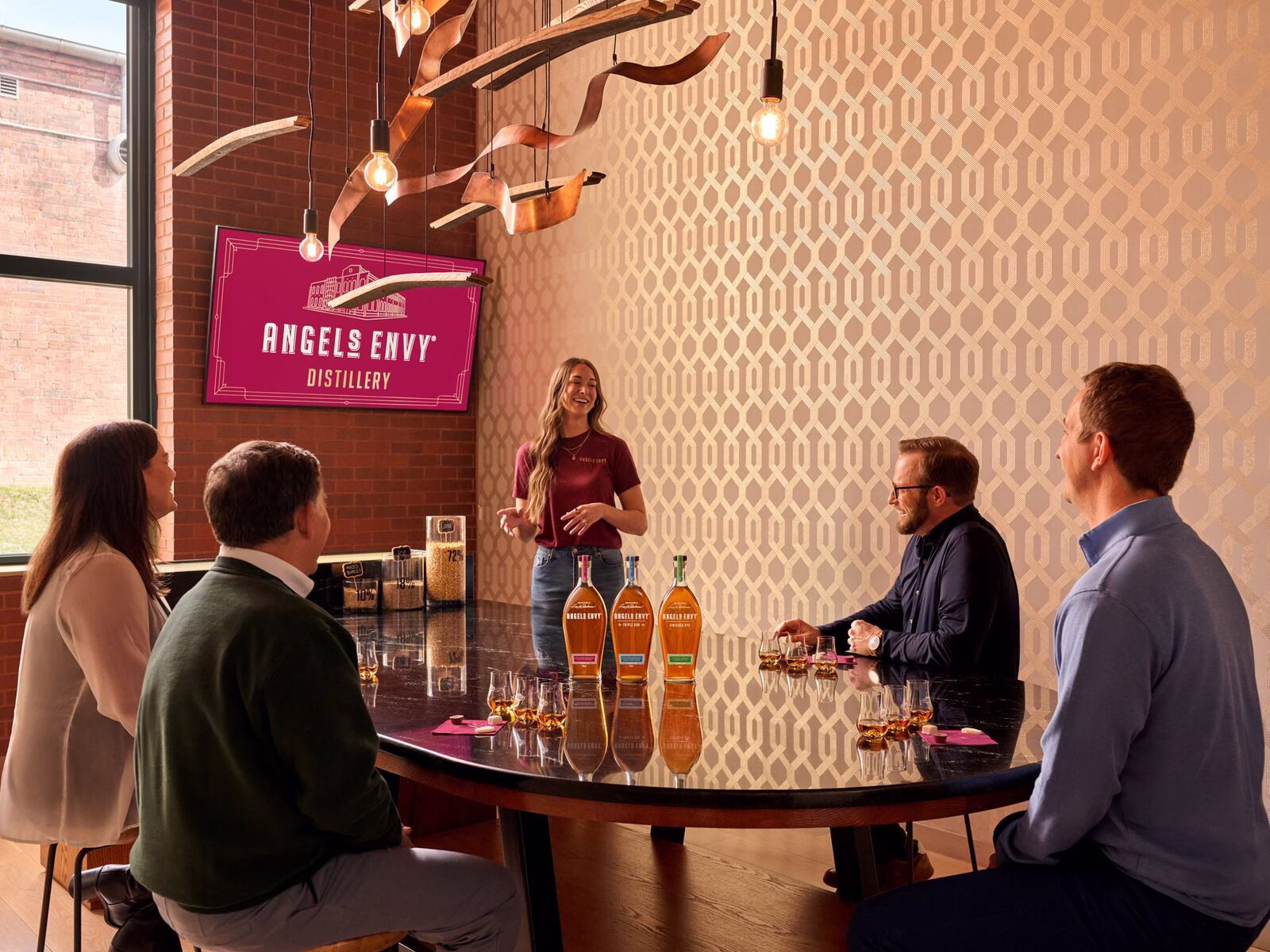 Candid photo of the Angel’s Envy Distillery tasting experience with a guide presenting three whiskey bottles to four guests around a table.