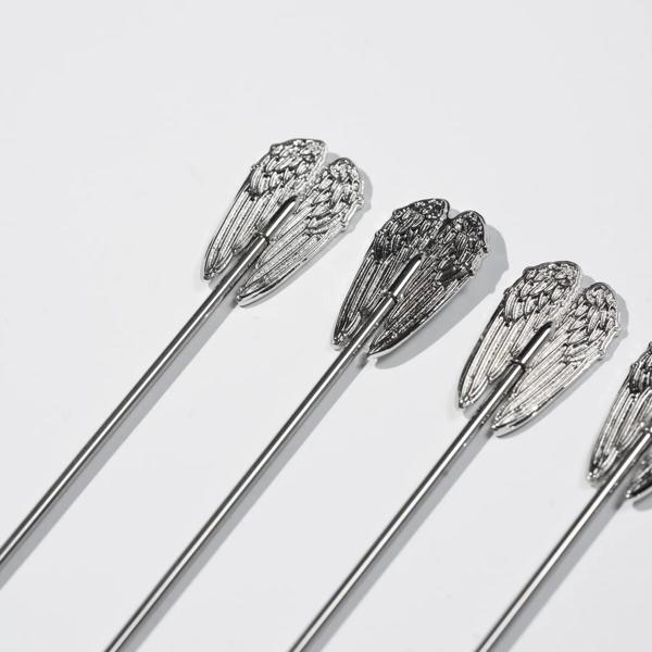 A set of four silver cocktail picks, each one topped with a detailed Angel’s Envy wing design.