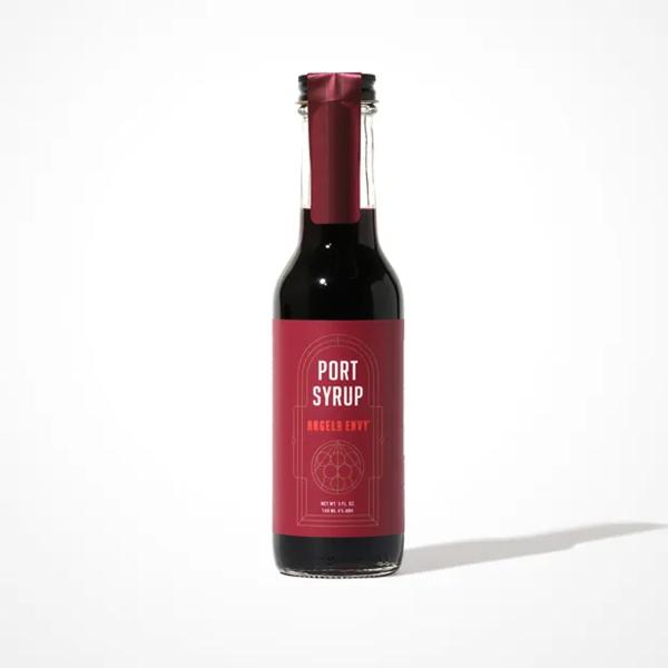 Five fluid ounces of Angel’s Envy Port Syrup in a glass bottle, with a deep burgundy label and matching neck wrap sealing the bottle’s cap.