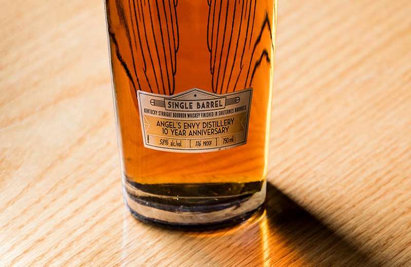 The lower-half of a decorative Angel’s Envy Singe Barrel Bourbon bottle with a label that reads “Angel’s Envy Distillery 10 year Anniversary”