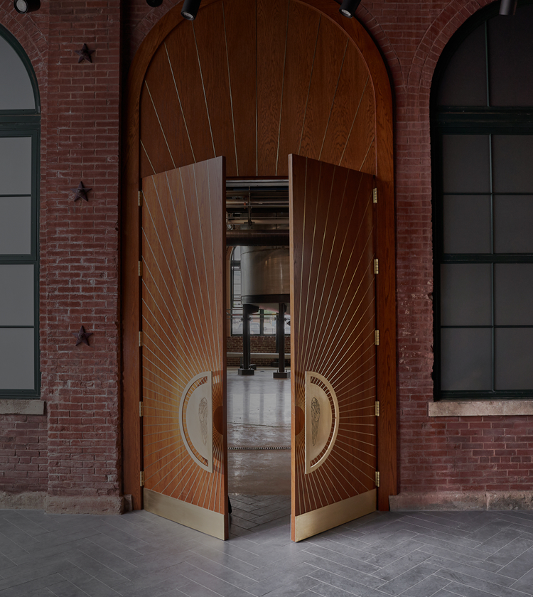 A set of gold-plated, wooden double doors, resting ajar and revealing a view inside the Angel’s Envy distillery.