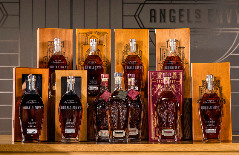 Eleven bottles of Angel’s Envy Cask Strength Bourbon, each with a unique year on its label from 2016 to 2026. Most bottles are accompanied by a decorative box made of wood.